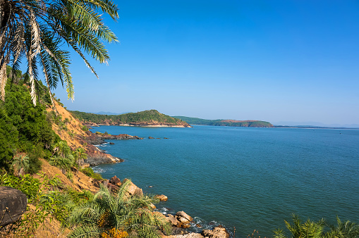 the scenery is beautiful rocky coast with palm tree, blue sea and cloudless sky in Om beach, Gokarna,