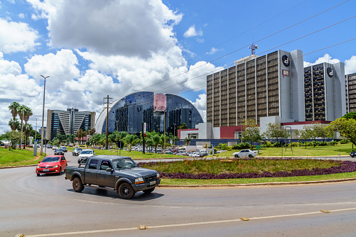 Brasilia, Brazil - February 23, 2017: Vehicles negotiating a roundabout in downtown Brasilia. Various buildings are pictured in the background and people are visible in the cars and in the background