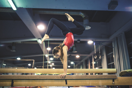 Low angle view of female gymnast performing on balance beam during practice in sports hall.