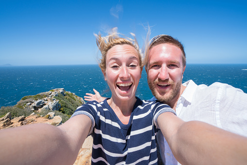 Two young adults taking a selfie portrait at the Cape of Good Hope in South Africa. It is located in Cape Peninsula near Cape Town. People travel concept.