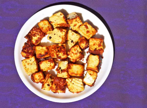 Fried paneer chunks classic and traditional Indian dish; on the blue background in white plate.