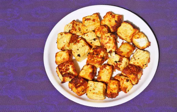 Fried paneer chunks classic and traditional Indian dish; on the blue background in white plate.