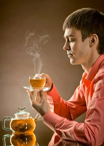 vertical closeup portrait  the  beautiful man hold cup with green  tea,  on brown background