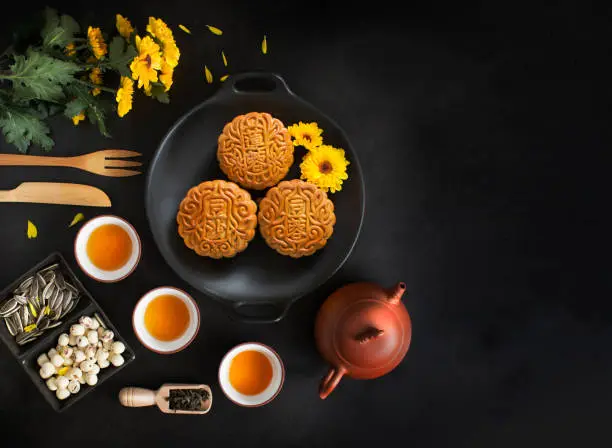 Overhead view mid autumn mooncake and tea set on black texture table top background. Text space image.