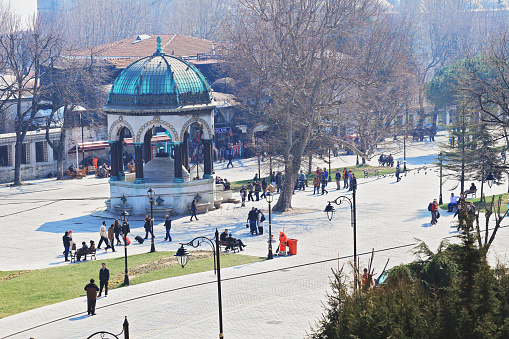 Some people walking to mosque and the others are near the German Fountain which planned neo-Byzantine style is in the northern end of Sultanahmet Square, Istanbul, Turkey on March 21, 2012