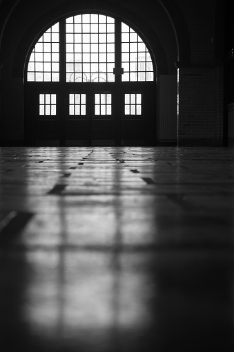 Light streams through windows at the Liberty State Park railroad and ferry terminal creating a beautiful silhouette. Image is black and white.