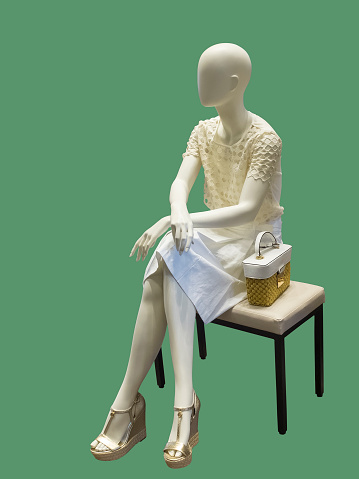 Sitting female mannequin against green background. No brand names or copyright objects.