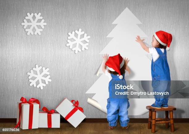 Little Twins Dressed Santa Hat Glue Christmas Tree On Wall At Home Xmas Concept Stock Photo - Download Image Now
