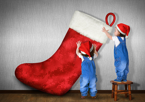 Little twins dressed Santa hat, hangs big Christmas stocking for gifts, xmas concept