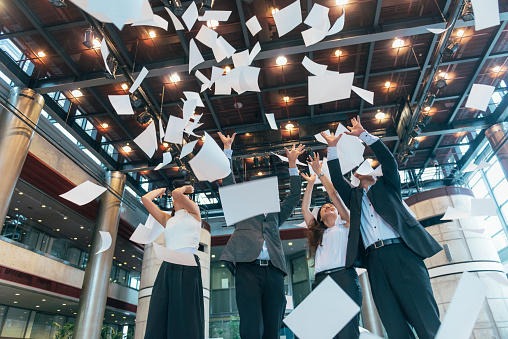 Japanese business people in corporate office throwing papers and documents during office party and achieved success in business