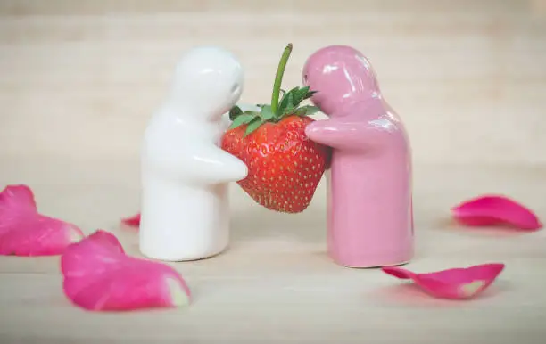 Ceramic toys giving a strawberry to couple for their love,  romantic background (vintage effect)
