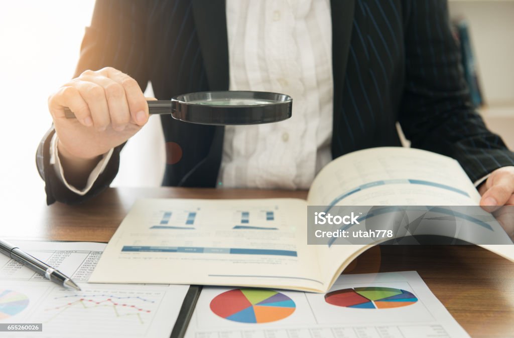 auditing Business women using magnifying to review financial summary report. Concept of Internal audit, Auditing tax,  Analyze return on investment. Internal Revenue Service Stock Photo