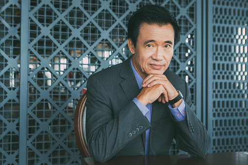 Portrait of mature Asian businessman with hands under chin sitting in restaurant and looking at camera