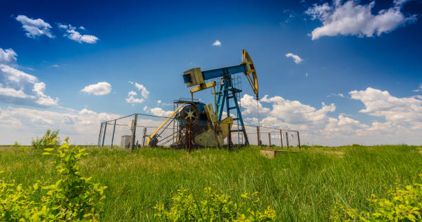 campo de petróleo com jack bomba, perfilado em céu azul com nuvens brancas, em um dia ensolarado - oil pump oil industry alberta equipment - fotografias e filmes do acervo