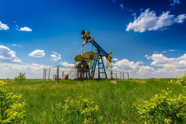 oil field with pump jack, profiled on blue sky with white clouds, on a sunny day - oil pump oil industry alberta equipment imagens e fotografias de stock