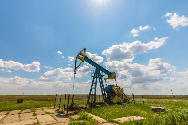 oil field with pump jack, profiled on blue sky with white clouds, on a sunny day - oil pump oil industry alberta equipment imagens e fotografias de stock