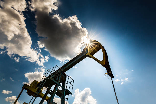oil field with pump jack, profiled on blue sky with white clouds, on a sunny day - oil pump oil industry alberta equipment imagens e fotografias de stock