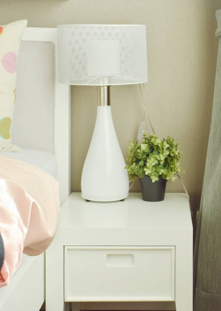istock White lamp and flower pot on bedside table next to bed 655292900