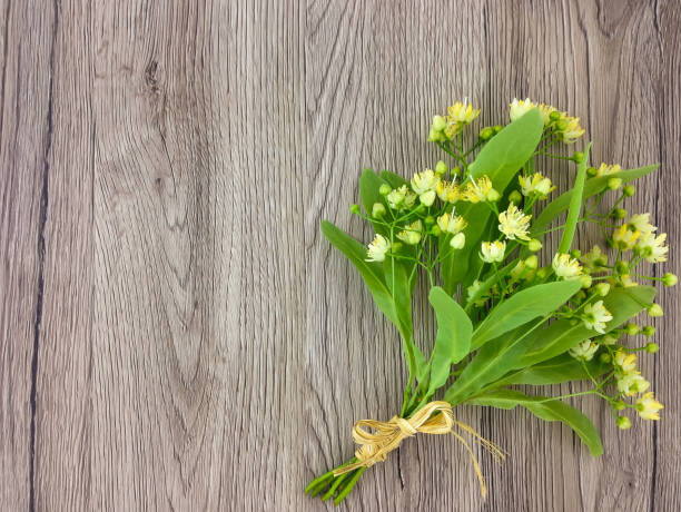 Minimal still life with linden flowers bouquet on a wooden table. Summer cozy composition, rustic holiday concept. Flat lay, top view, space for text