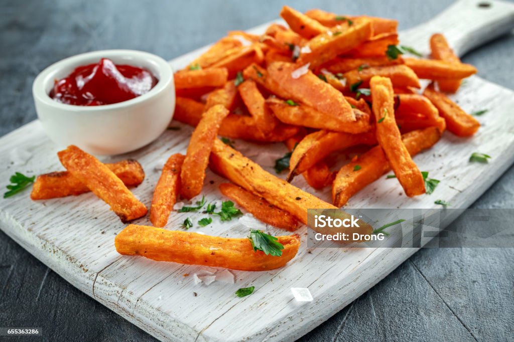 Healthy Homemade Baked Orange Sweet Potato Fries with ketchup, salt, pepper on white wooden board Healthy Homemade Baked Orange Sweet Potato Fries with ketchup, salt, pepper on white wooden board. French Fries Stock Photo