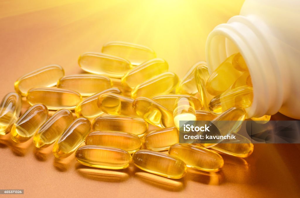 Fish oil and vitamin D softgels Fish oil capsules with omega 3 and vitamin D in a plastic bottle on a shiny texture with sun beams, healthy diet concept Vitamin D Stock Photo