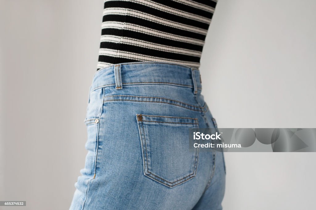 Menina vestida de jeans azul e listrado t-shirt, vista lateral. Copie o espaço. Fundo branco. - Foto de stock de Cintura alta royalty-free
