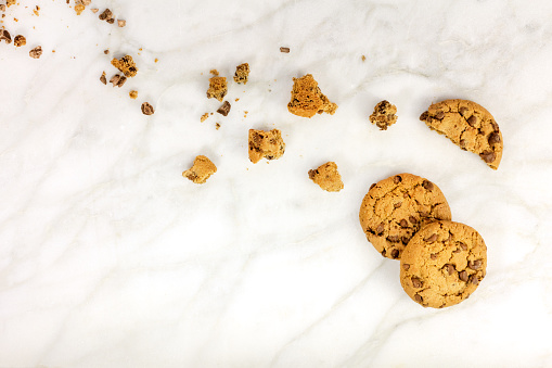 Chocolate chips cookies and crumbs, shot from above on a white marble background, with a place for text