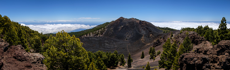 Panoramic image of Lava field Malforado and the crater of vocano Duraznero on Ruta de los Volcanes, Cumbre Vieja, La Palma, Spain. Pico de  Teide volcano on Tenerife visible above the clouds in the background