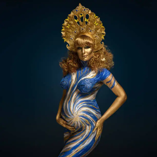 Fashionable redhead pregnant woman with kokoshnik and abstract body art in shades of blue and gold