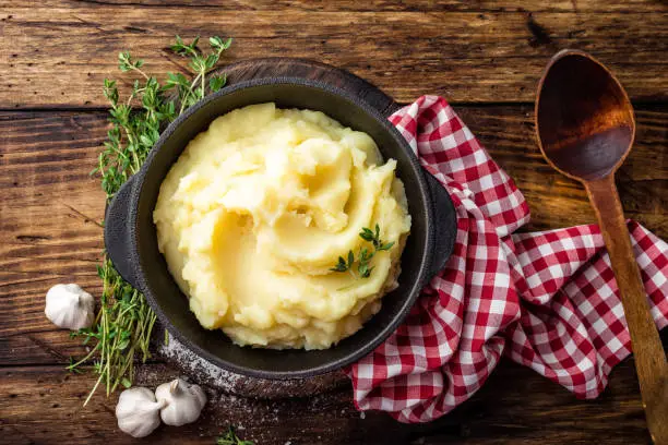 Photo of Mashed potatoes, boiled puree in cast iron pot on dark wooden rustic background, top view