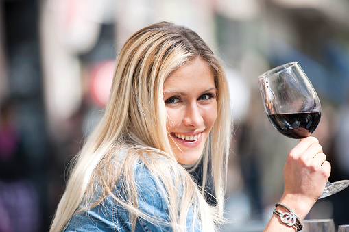 Woman with wineglass half full with red wine, outdoors, looking at camera