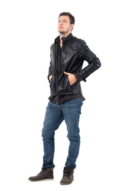 istock Young serious casual man in leather jacket with hands in pockets looking up 655476360