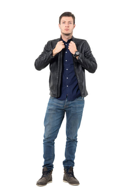 Serious young man adjusting collar of leather black jacket looking at camera