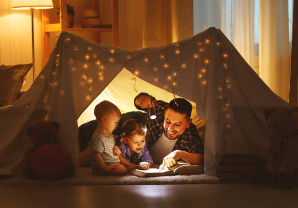 felice padre di famiglia e figli leggendo un libro in tenda a casa - padre single foto e immagini stock