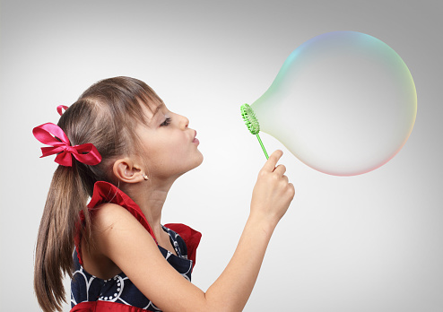 Portrait of child girl blowing big soap bubble, studio shot