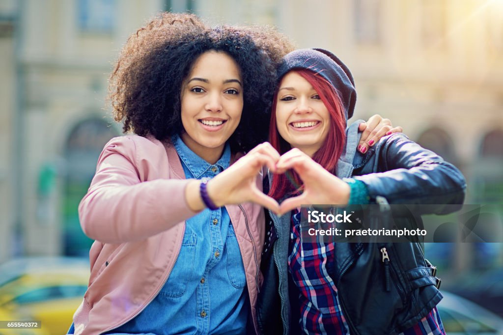 Two girlfriends making heart with their hands on the street Heart Shape Stock Photo