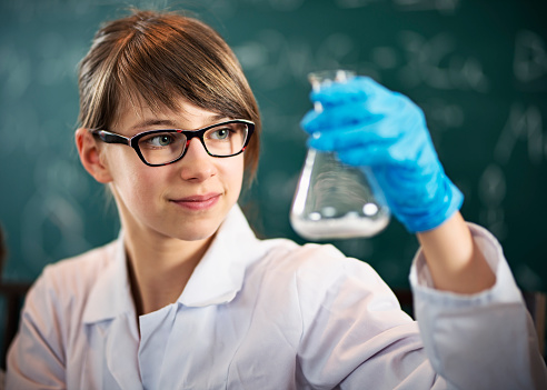 Portrait of teenage girl in chemistry class holding a conical flask. The flask has some white powder inside.