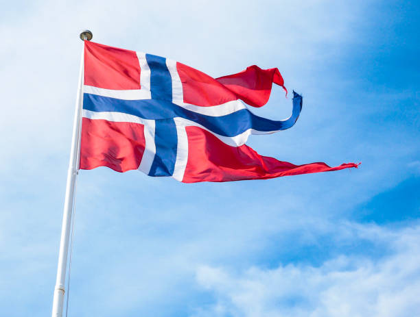 The Royal flag of Norway on a pole towards blue and white sky in daylight stock photo