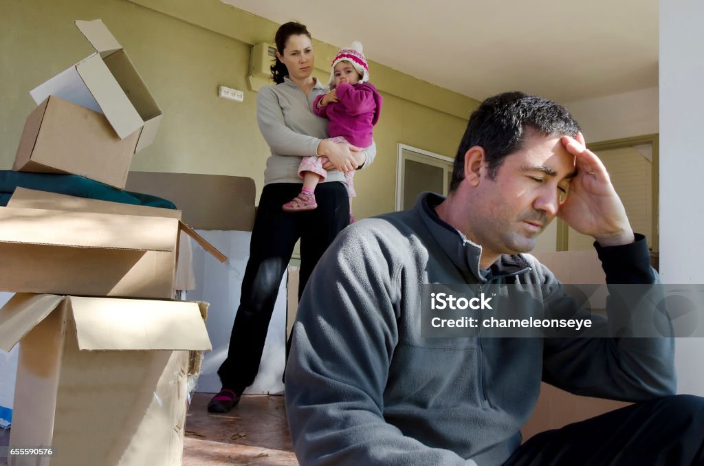 Concept Photo - Divorce, Eviction, Financial or Family Issues Young parents and their daughter stand beside cardboard boxes outside their home. Concept photo illustrating divorce, homelessness, eviction, unemployment, financial, marriage or family issues. Family Stock Photo