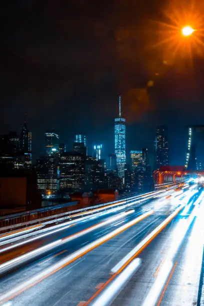 Long Exposure photo of cars driving across Brooklyn Bridge with world tower seen in the background on a dark gloomy night in New York.