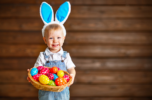 Happy baby boy in Easter bunny suit with a basket of eggs