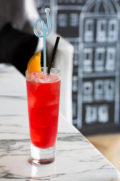 Red color cocktail decorated with piece of orange