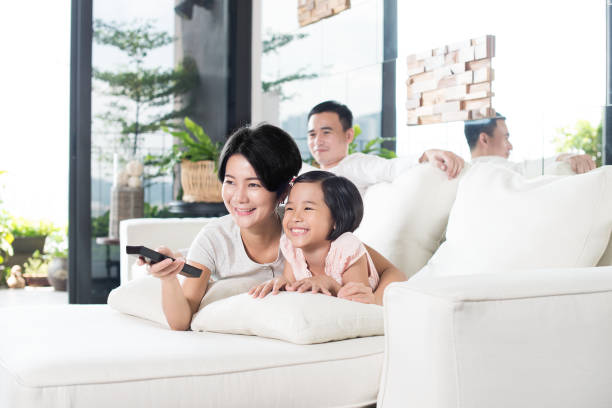 Young Asian family watching TV at home. Young Asian parents with only child watching television on the sofa in the living room. asian kids watching tv stock pictures, royalty-free photos & images