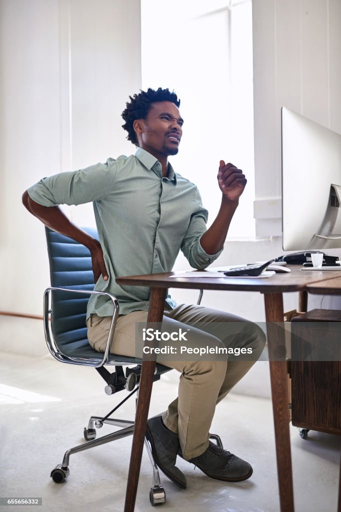 Poor posture can lead to unbearable pain Shot of a young designer suffering from back pain while working at his desk in an office Full Length Stock Photo