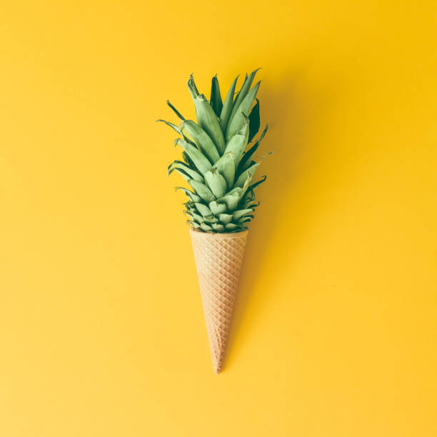 Ice cream cone with pineapple leaves on bright yellow background. Fruit and candy concept. Flat lay.