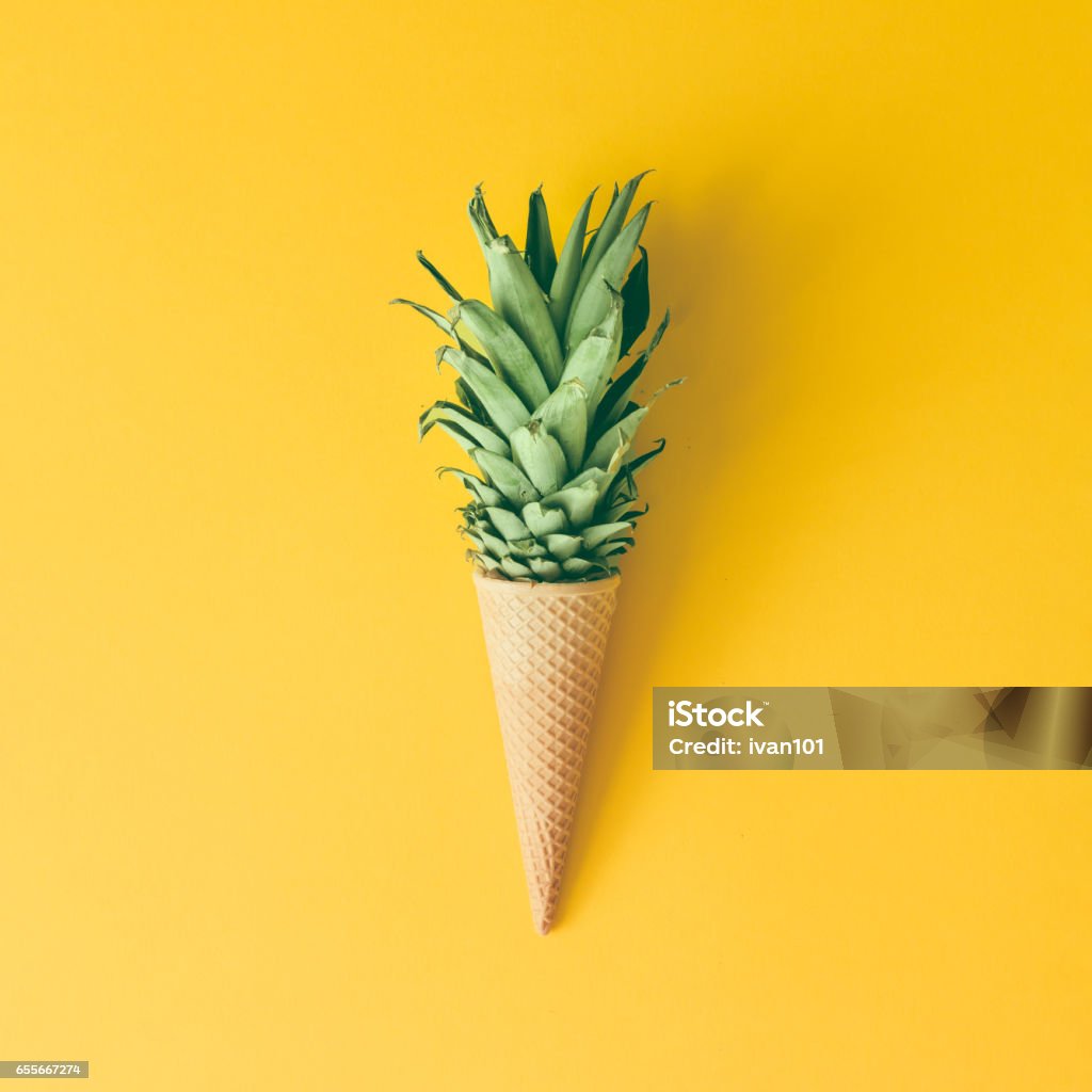 Ice cream cone with pineapple leaves on bright yellow background. Fruit and candy concept. Flat lay. Fruit Stock Photo