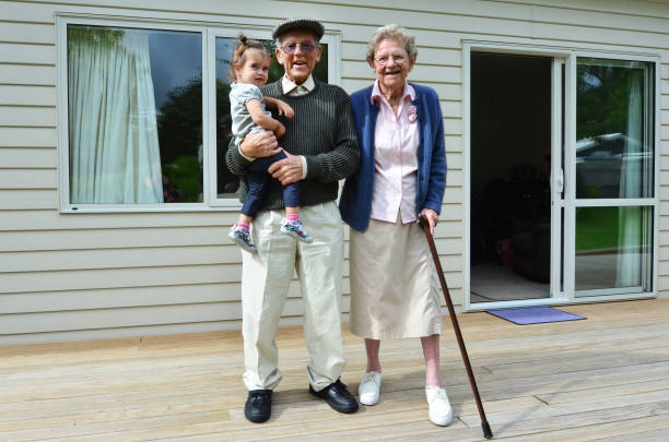 Smiling grandparents holding their grandchild outside their home.