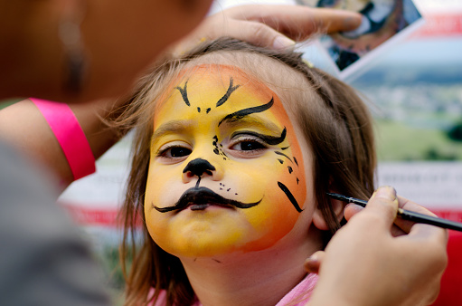Cute little girl with face painted like a lion.