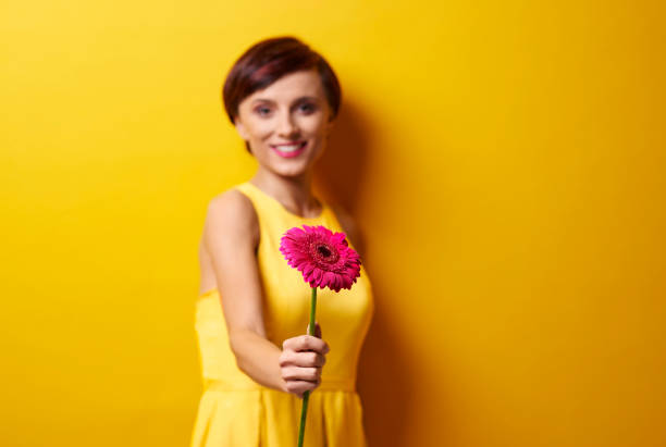 A blissful woman embraces a bouquet of pink flowers wrapped in brown paper, standing in a bustling urban environment and radiating joy and contentment as she closes her eyes.