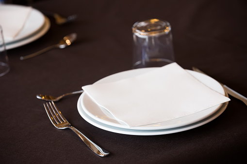 Dining set of empty white plate, knife, fork and glass on the table in the restaurant